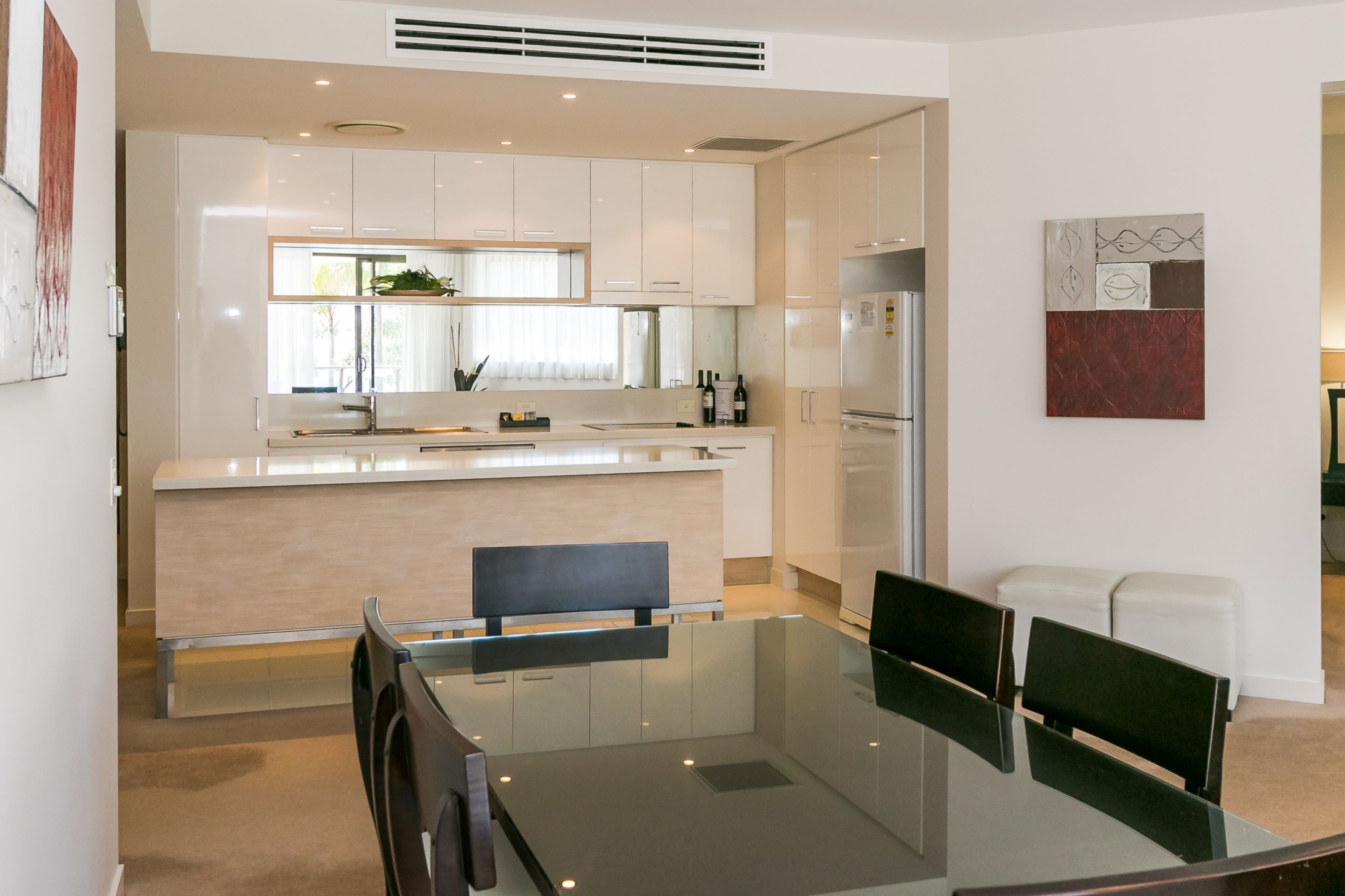 A modern kitchen with white cabinets, a central island, and a dining area with a glass table and chairs.