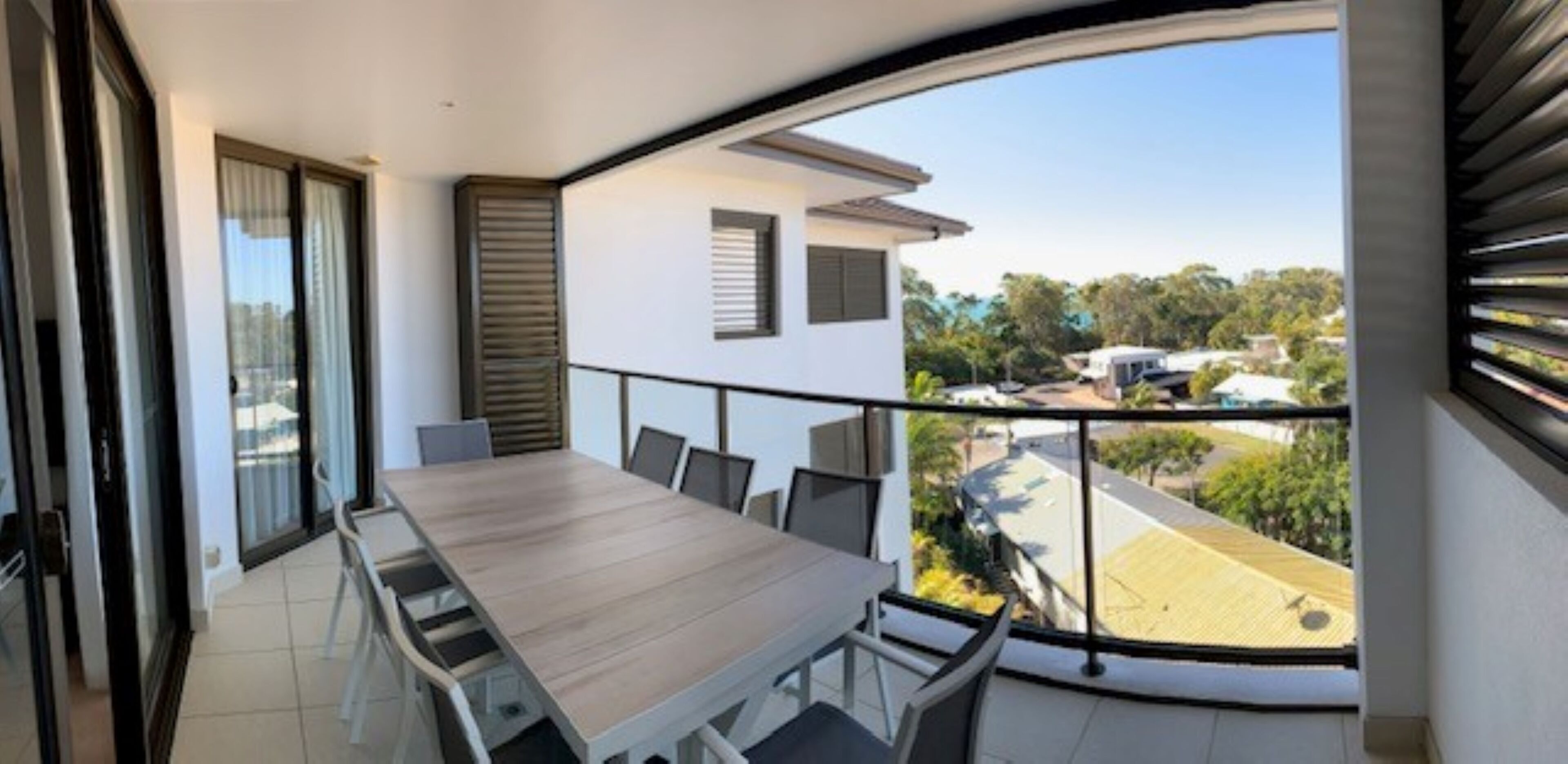 A modern balcony with a wooden table and chairs, offering a view of the surrounding neighborhood.