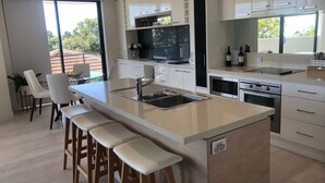 Una cocina moderna con una isla central, taburetes de bar, armarios blancos y un amplio ventanal con vistas al exterior.
