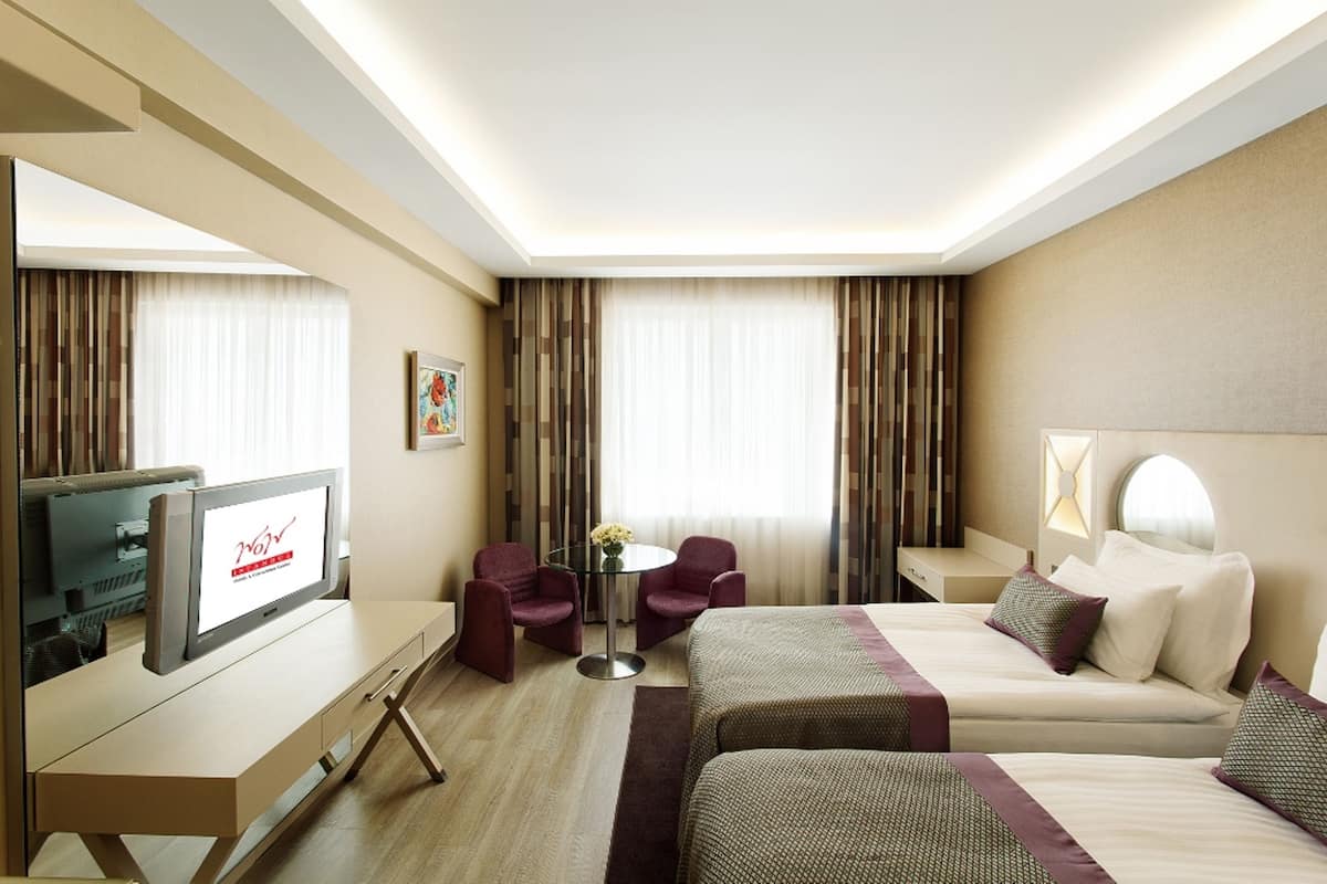 A hotel room with a TV, two beds, a desk, and a small table with chairs.