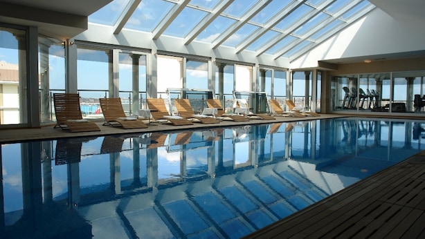 A large indoor swimming pool with clear glass walls, wooden deck, and sun loungers. - WOW Istanbul Hotel (Istanbul)