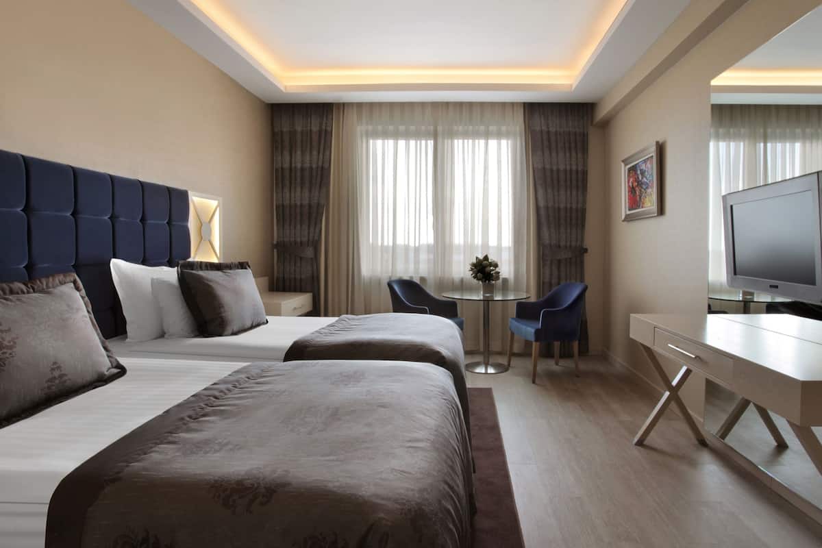 A hotel room with two beds, a desk, a TV, and a small table with chairs.