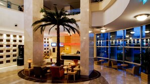 A lobby with a palm tree, seating areas, a reception desk, and a large window with a view. - WOW Istanbul Hotel (Istanbul)