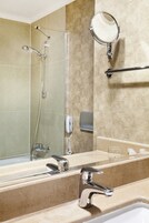 A bathroom with a large mirror, a handheld showerhead, a handheld shower, a towel rack, and a soap dispenser.