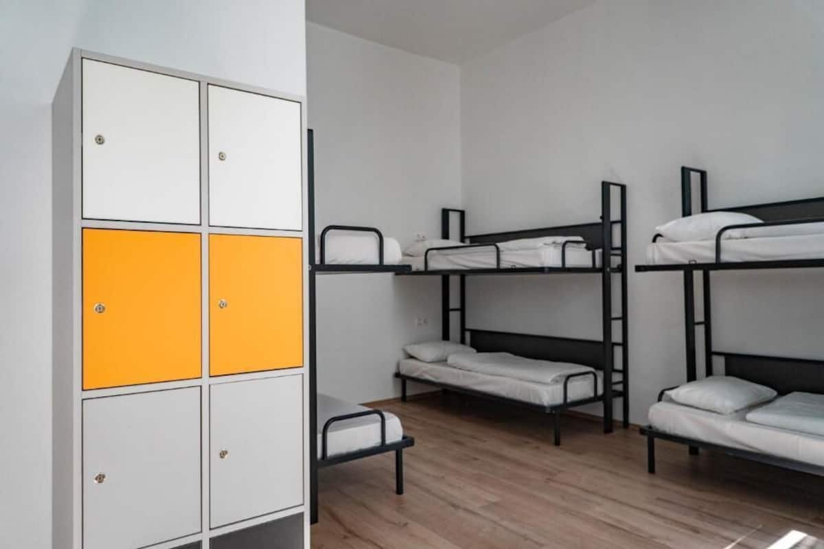 Une chambre de dortoir avec des lits superposés, une armoire avec des compartiments orange et blancs, et un plancher en bois.