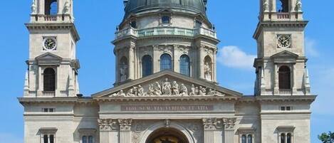 A large, historic building with a central dome and two bell towers, featuring classical architecture and a prominent entrance.