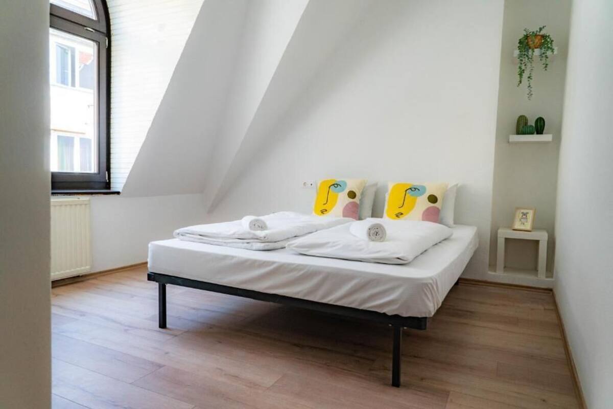 Une chambre avec un lit, une fenêtre et une petite étagère blanche ornée de plantes.