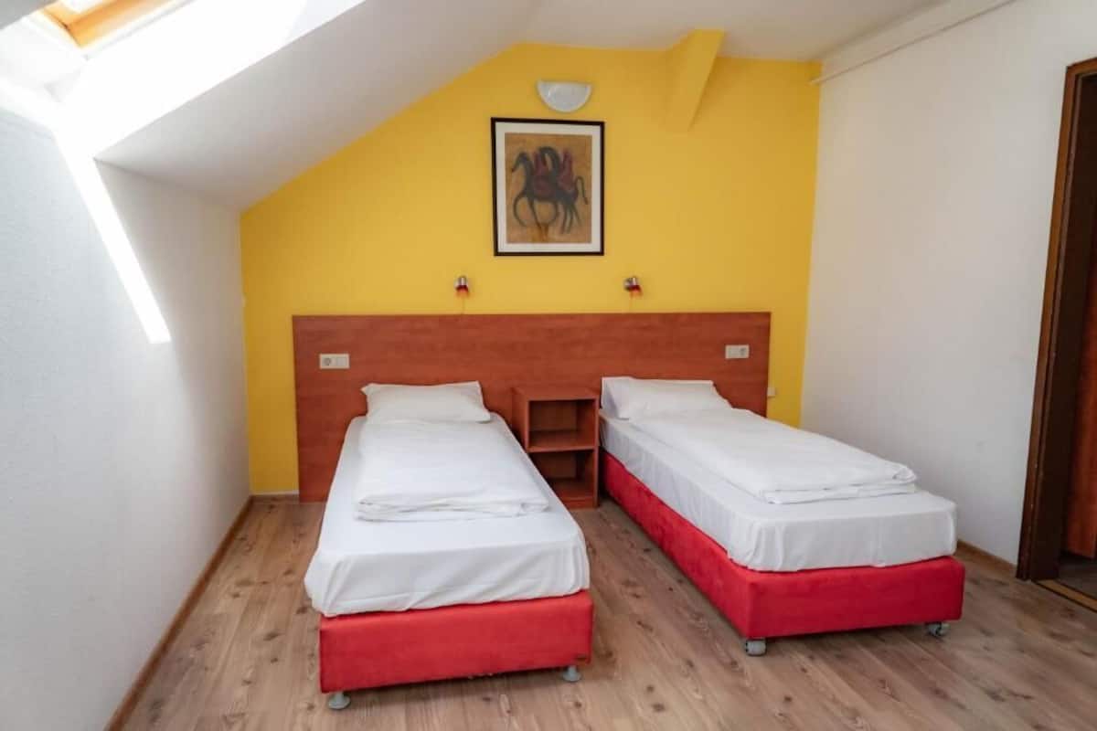 Une chambre avec deux lits, une tête de lit en bois, un mur jaune et un puits de lumière.