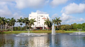 A hotel with a white exterior, palm trees, and a fountain in the foreground. - Hawthorn Extended Stay by Wyndham West Palm Beach Airport (West Palm Beach)