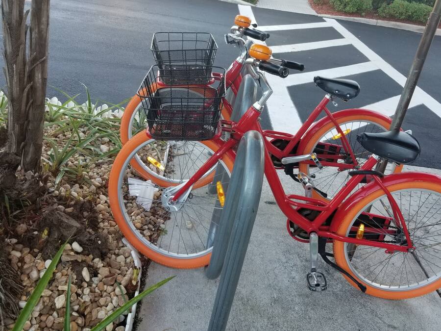 A red bicycle with a basket, parked on a sidewalk.