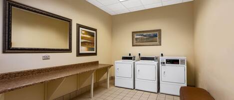 A laundry room with a bench, two washing machines, a countertop, and two framed pictures on the wall.
