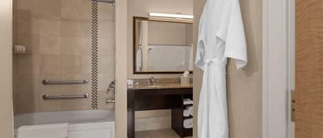 Un bagno moderno con vasca, doccia, mobile lavabo con specchio e un accappatoio appeso al muro.