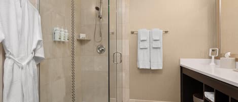 A modern bathroom with a glass-enclosed shower, a white bathtub, and a vanity with a mirror and towel rack.