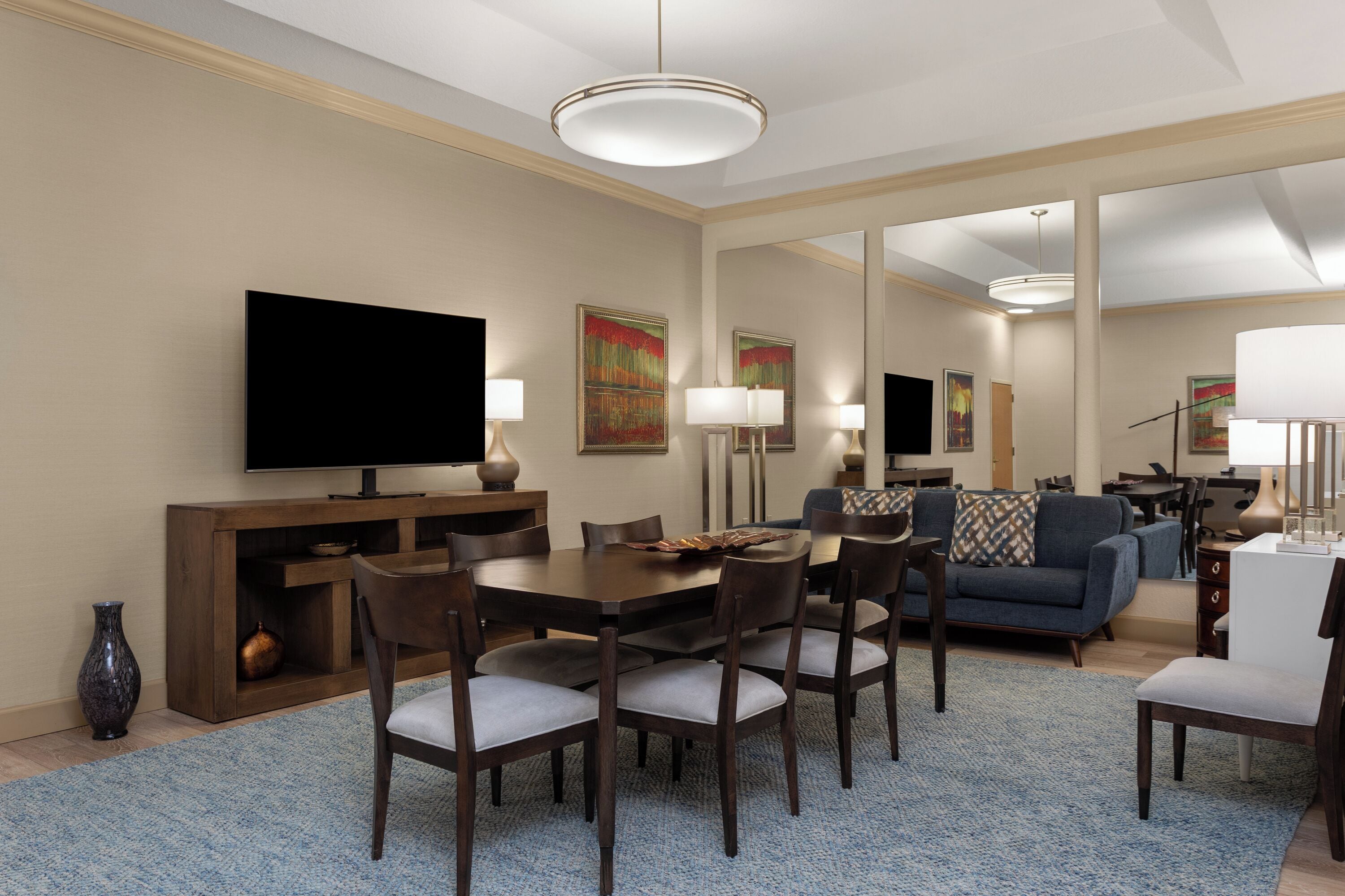A hotel room with a dining area, a TV, a sofa, and a large mirror.