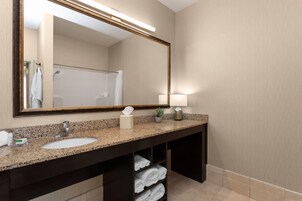 A bathroom with a granite countertop sink, a large mirror, a towel rack, and a shelf with folded towels.