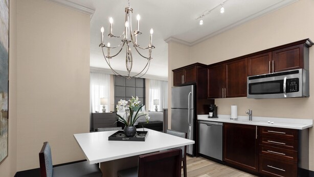 A modern kitchen with dark wooden cabinets, a stainless steel refrigerator, and a built-in microwave. - Hawthorn Extended Stay by Wyndham West Palm Beach Airport (West Palm Beach)