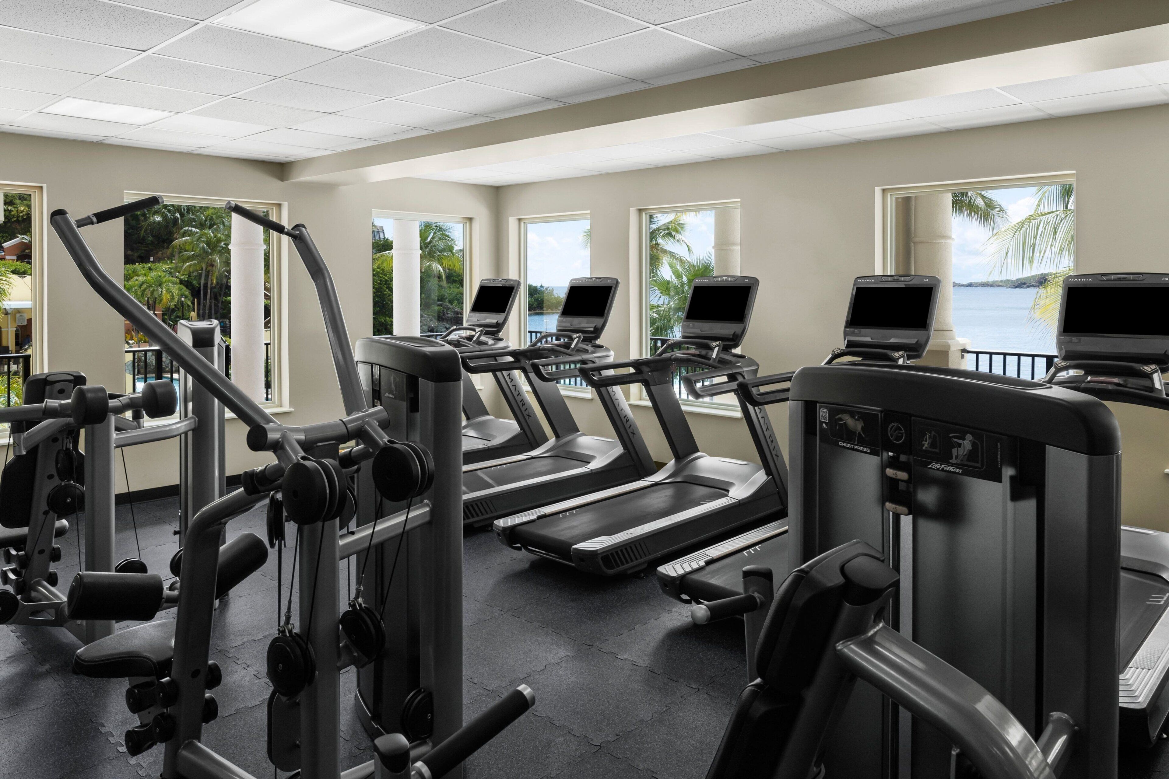 Une salle de sport équipée de tapis de course, d’appareils de musculation et offrant une vue sur l’océan.