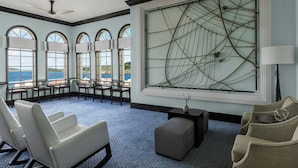 Habitación de hotel con un ventanal grande, ventilador de techo, zona de estar con sillones y un adorno en la pared.