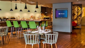 A modern restaurant with green chairs, a bar area, and a TV screen displaying the ESTELAR logo. - Estelar Apartamentos Bellavista (Lima)