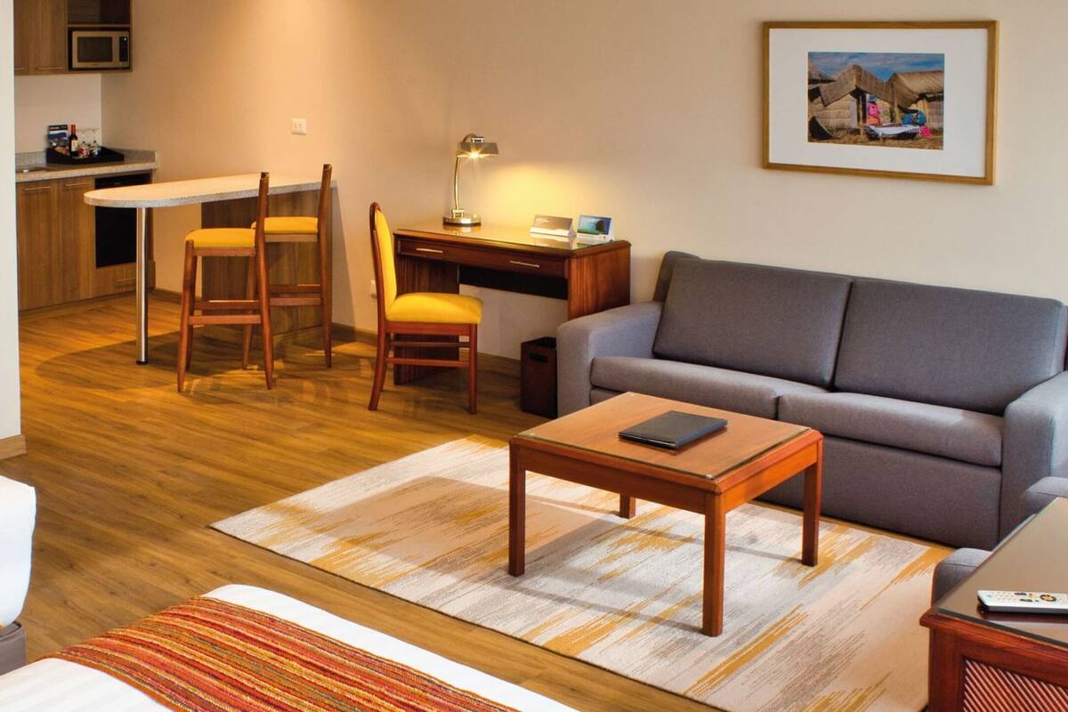 Hotelkamer met een bed, een slaapbank, een bureau met stoel, een kleine tafel en een kitchenette.