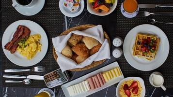 A breakfast setting with plates of eggs, bacon, waffles, and various fruits.