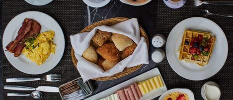 A breakfast setting with plates of eggs, bacon, waffles, and various fruits.