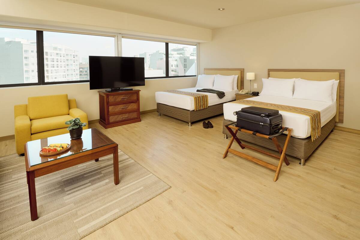 Een hotelkamer met een bed, een bank, een televisie, een bureau en een raam met uitzicht op de stad.