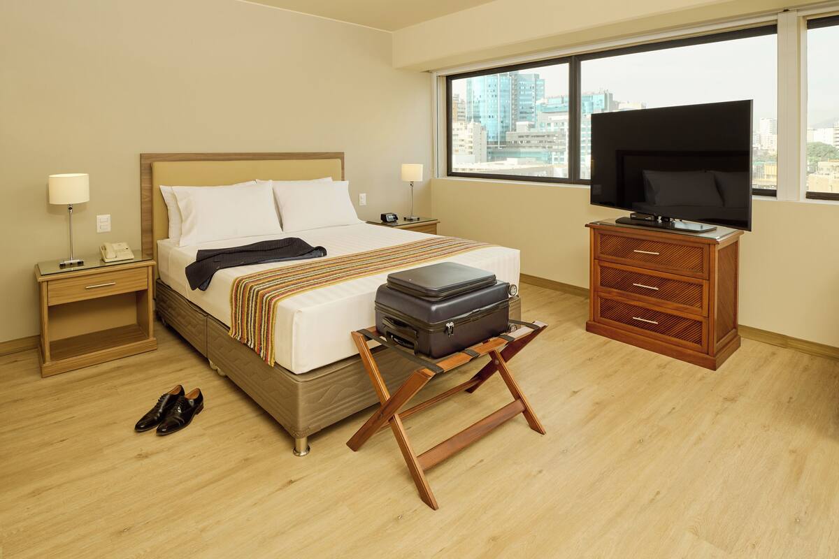 Een hotelkamer met een bed, een televisie, een dressoir, een koffer en een paar schoenen.