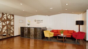 A reception area with a wooden reception desk, a yellow armchair, a red sofa, and a black floor lamp. - Estelar Apartamentos Bellavista (Lima)