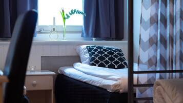 A bedroom with a bed, a nightstand, a window with curtains, and a radiator.