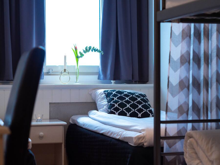 A bedroom with a bed, a nightstand, a window with curtains, and a radiator.