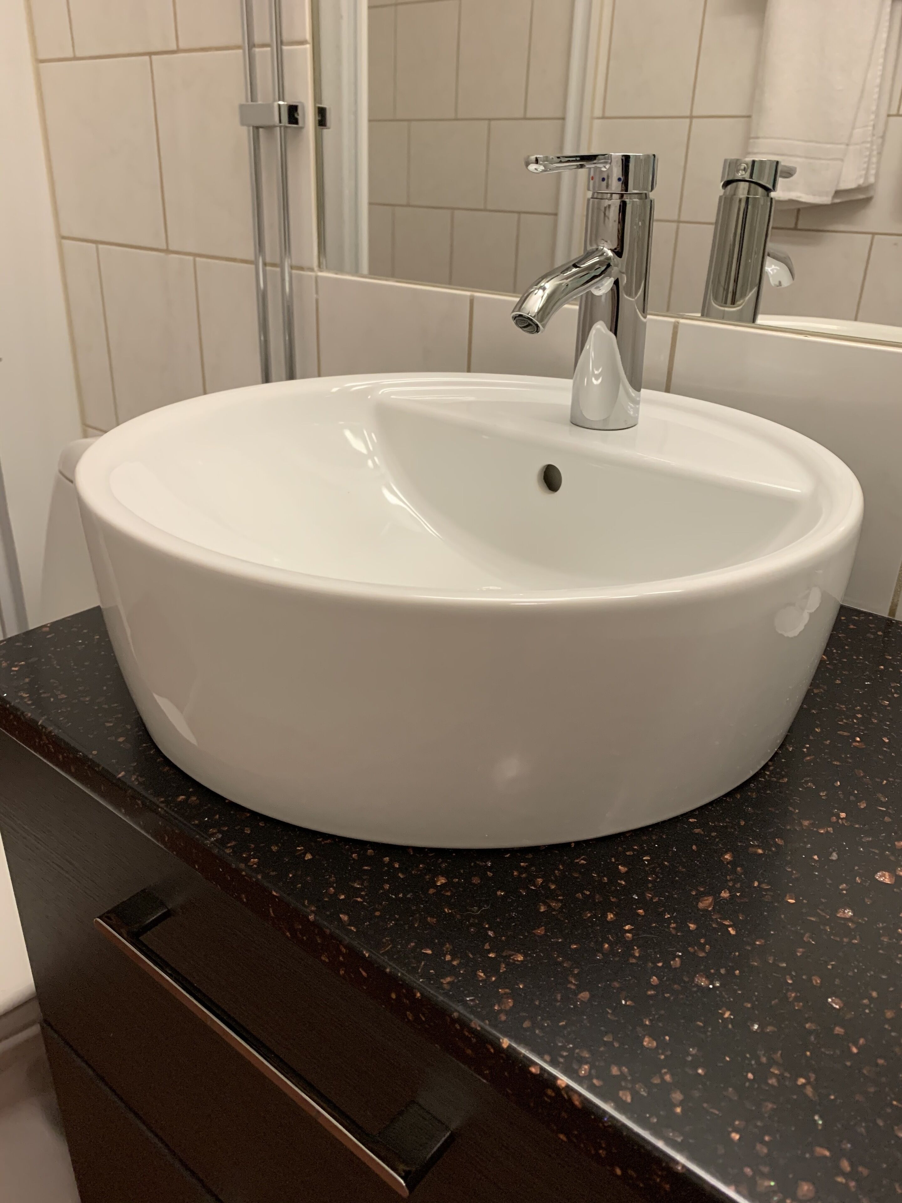 A white bathroom sink with a modern faucet, a dark speckled countertop, and a mirror above the sink.