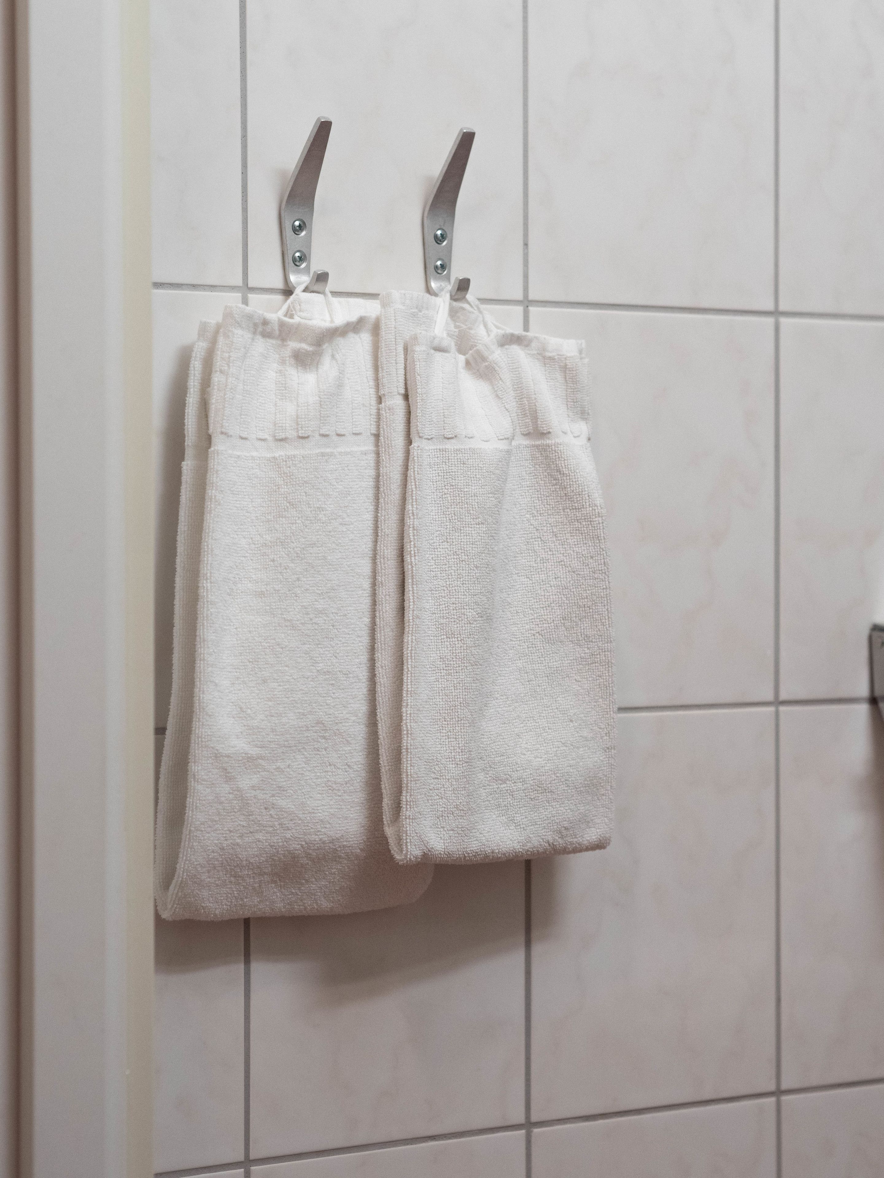 Two white towels hanging on a metal towel rack against a tiled wall.