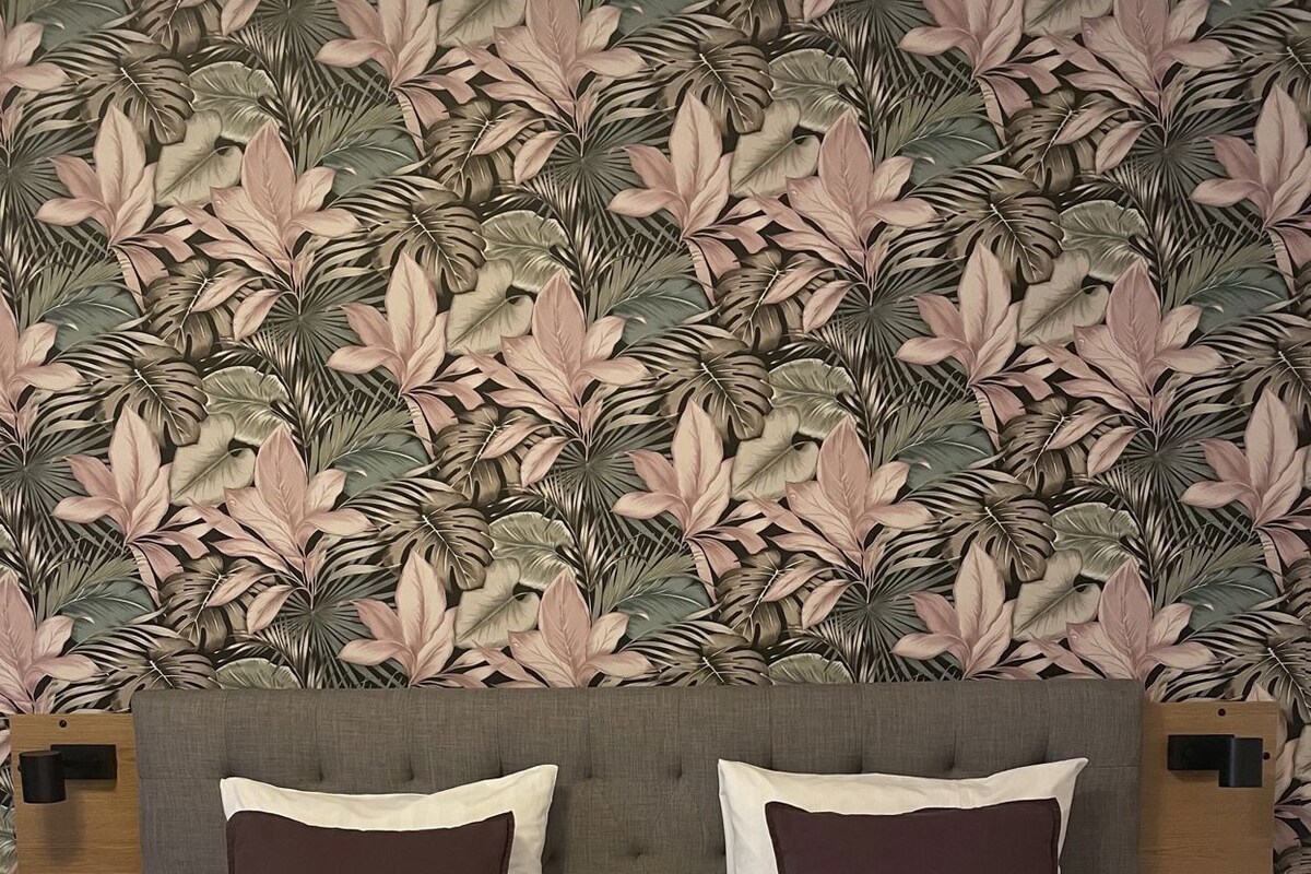 Una cama con cabecera, dos almohadas y un fondo de papel tapiz estampado.