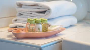 Un baño con una pila de toallas blancas, una bandeja rosa con botellas etiquetadas 'bamboo' y una botella de vidrio al fondo.