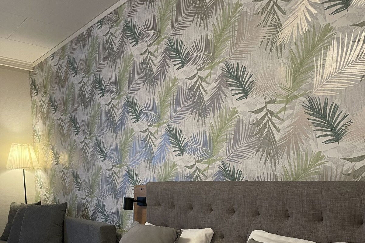 A hotel room with a large bed, two pillows, a headboard, and a wall with a leaf pattern.