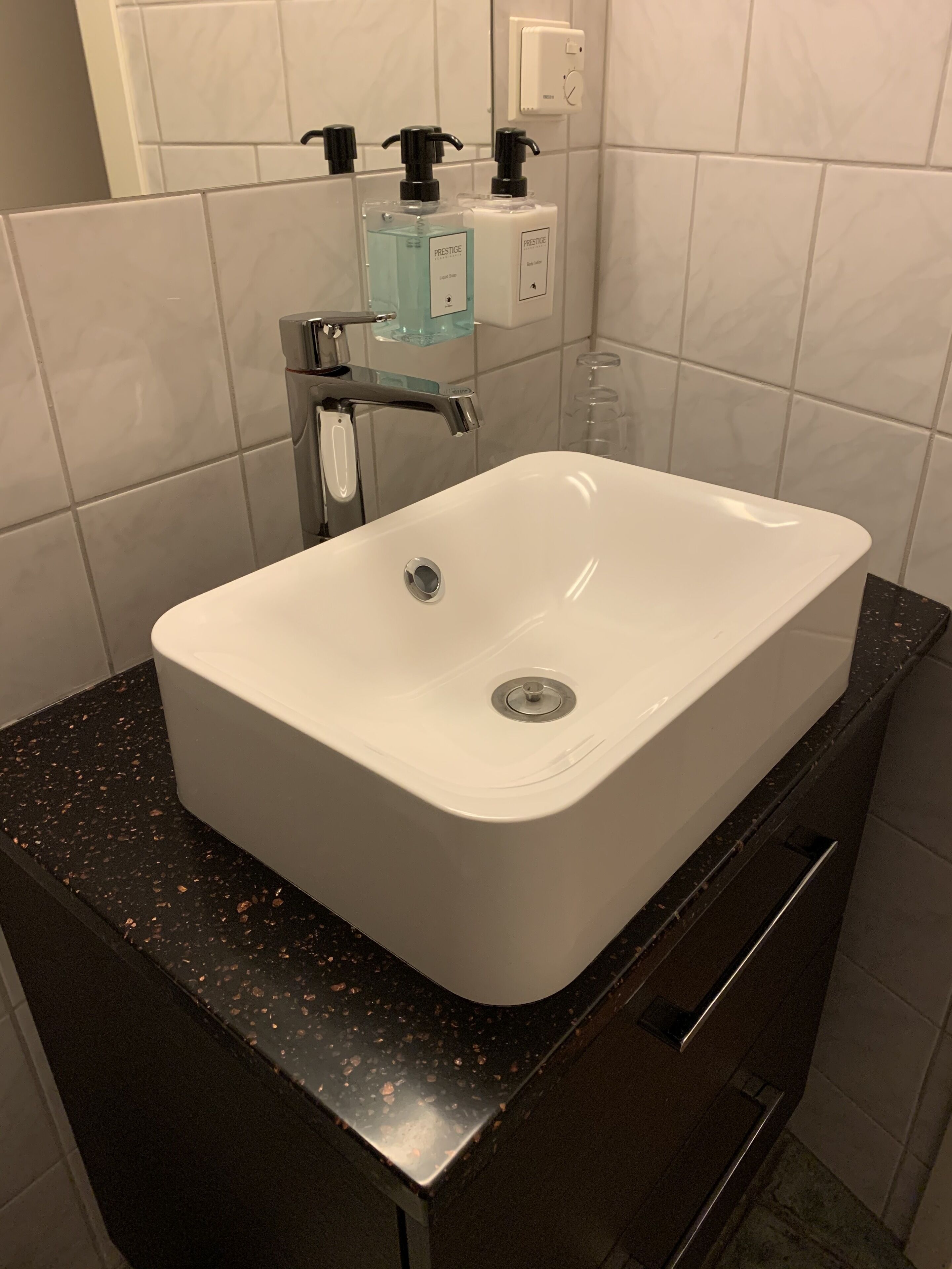 Un baño con lavamanos blanco, encimera negra y paredes cubiertas de azulejos blancos.