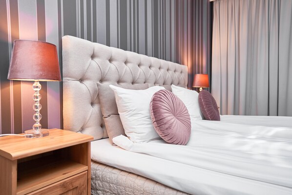 A neatly made bed with a tufted headboard, two bedside lamps, and a wooden nightstand with a drawer.