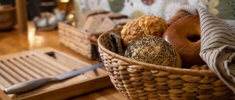 A basket of various breads and a cutting board with a knife on a wooden table.