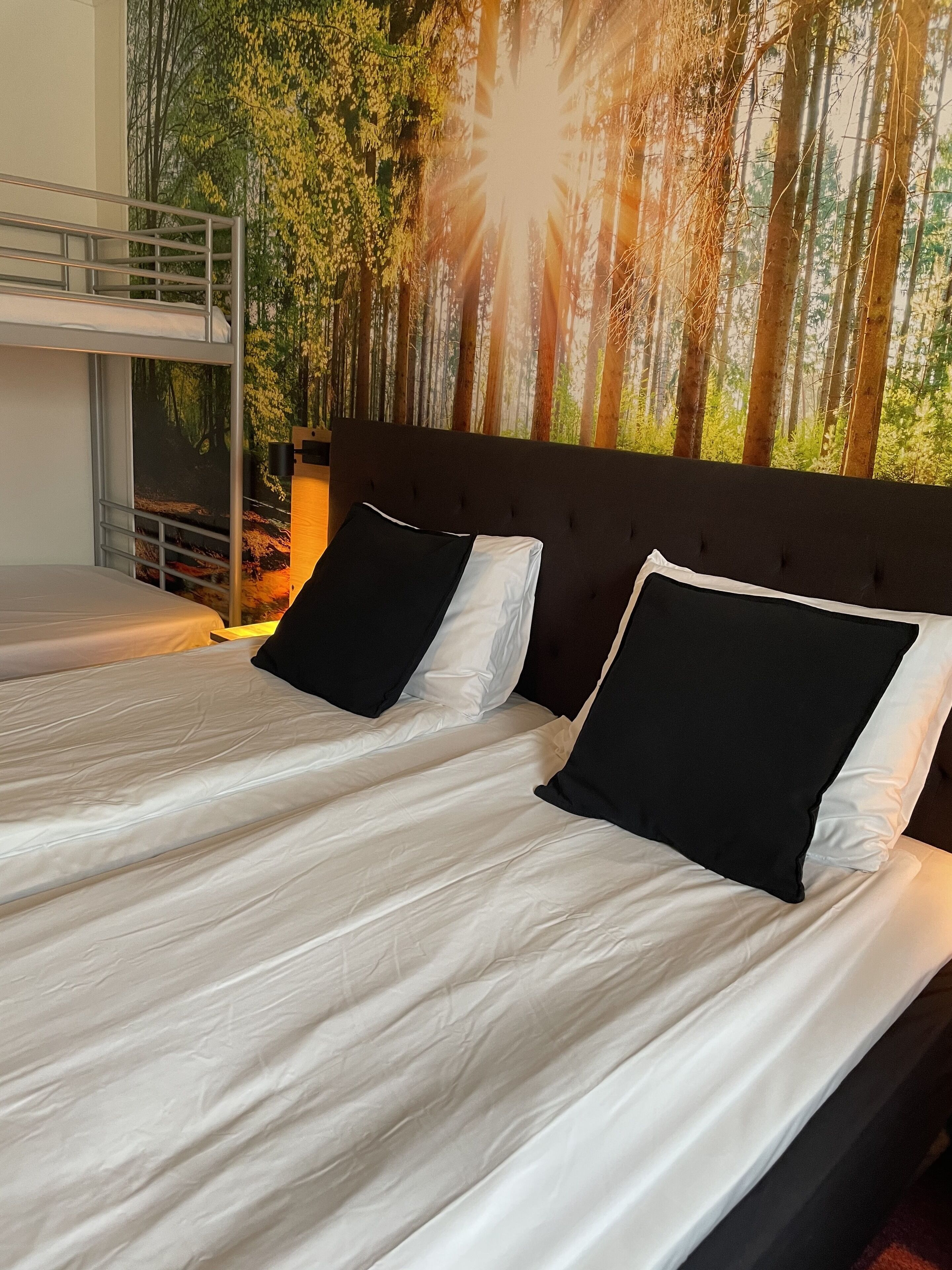 A room with a bunk bed and a single bed, both with white bedding and black pillows.
