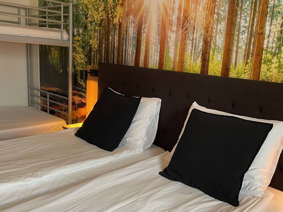 A room with a bunk bed and a single bed, both with white bedding and black pillows.