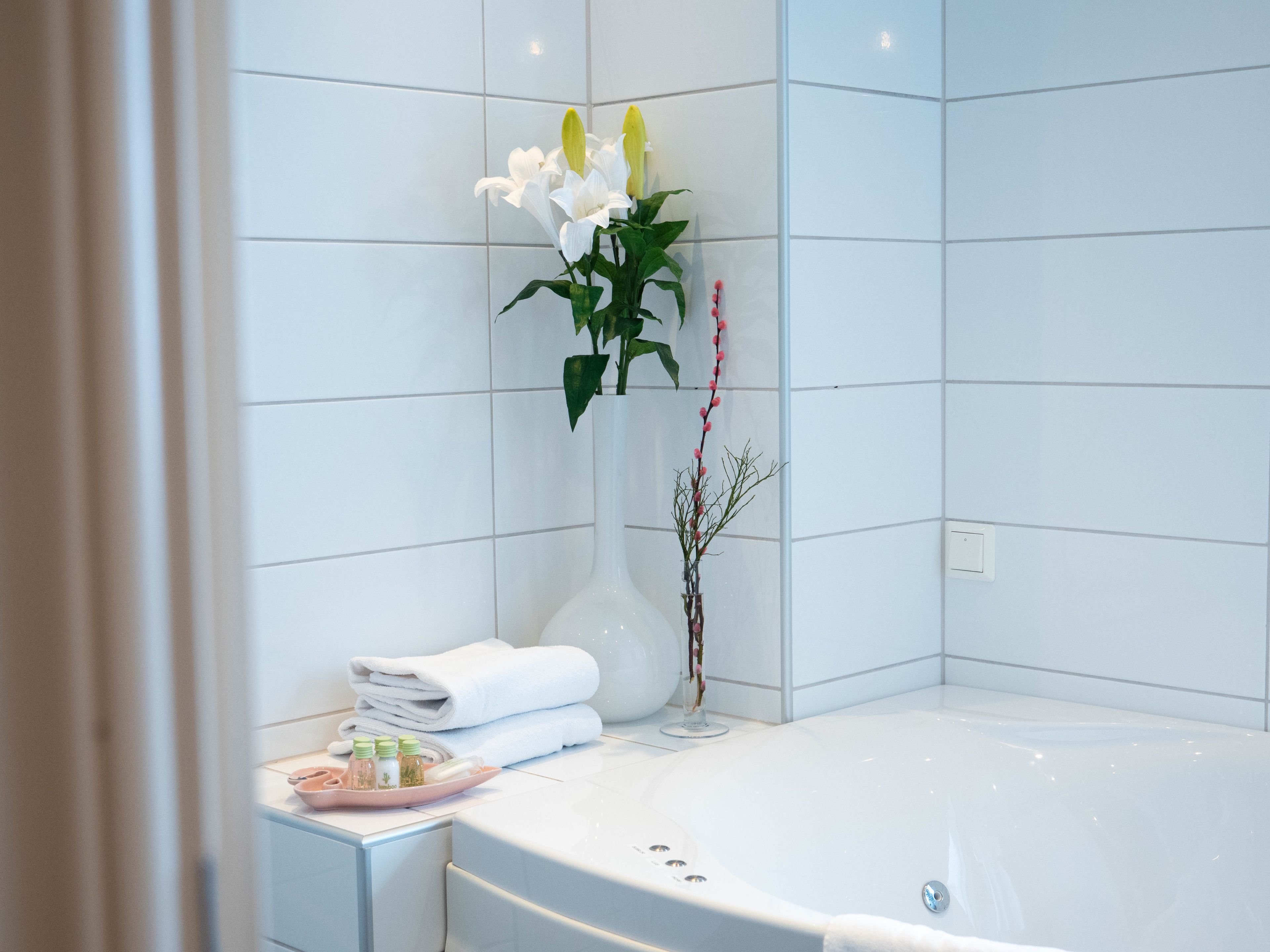 A modern bathroom with a white bathtub, a vase with white and yellow flowers, and a small plant.