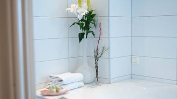 A modern bathroom with a white bathtub, a vase with white and yellow flowers, and a small plant.