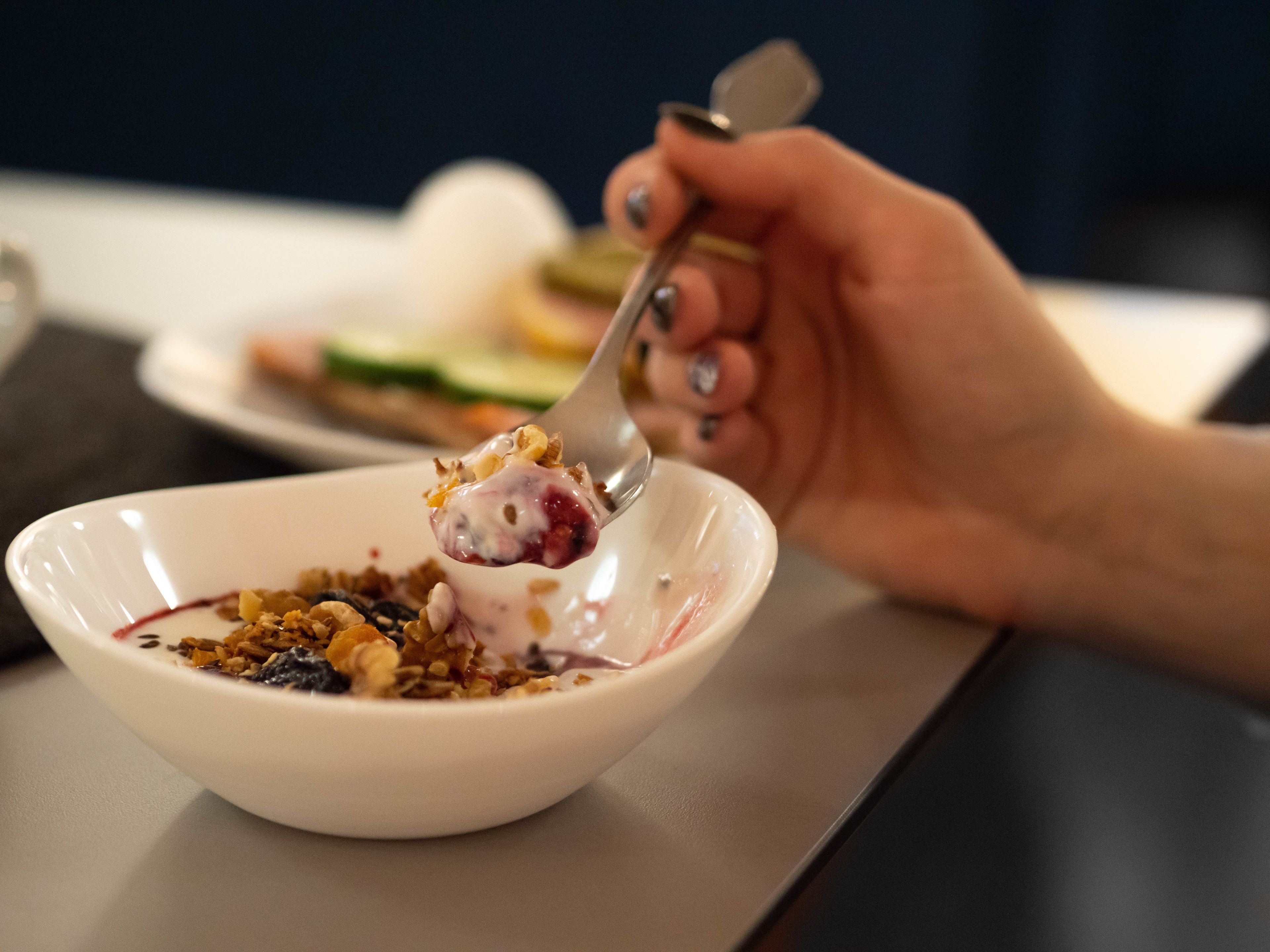 Egy tál joghurt, müzli és bogyós gyümölcsök, amit egy kanállal esznek.