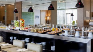 A buffet area with various food items, including fruits, pastries, and beverages, and a seating area with tables and chairs. - AC Hotel Brescia by Marriott (Brescia)