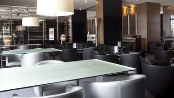 A modern hotel lobby with glass tables, black leather chairs, and large pendant lights.