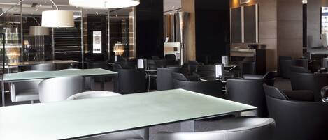 A modern hotel lobby with glass tables, black leather chairs, and large pendant lights.