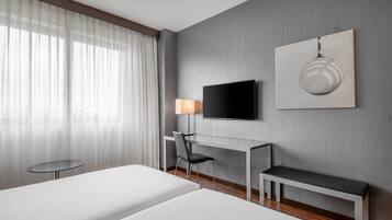 Ein Hotelzimmer mit zwei Betten, einem Schreibtisch, einem Sessel, einem Fernseher und einem Bild an der Wand.