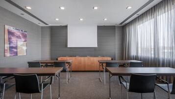 A conference room with a long table, chairs, a projector screen, and a large window with curtains.