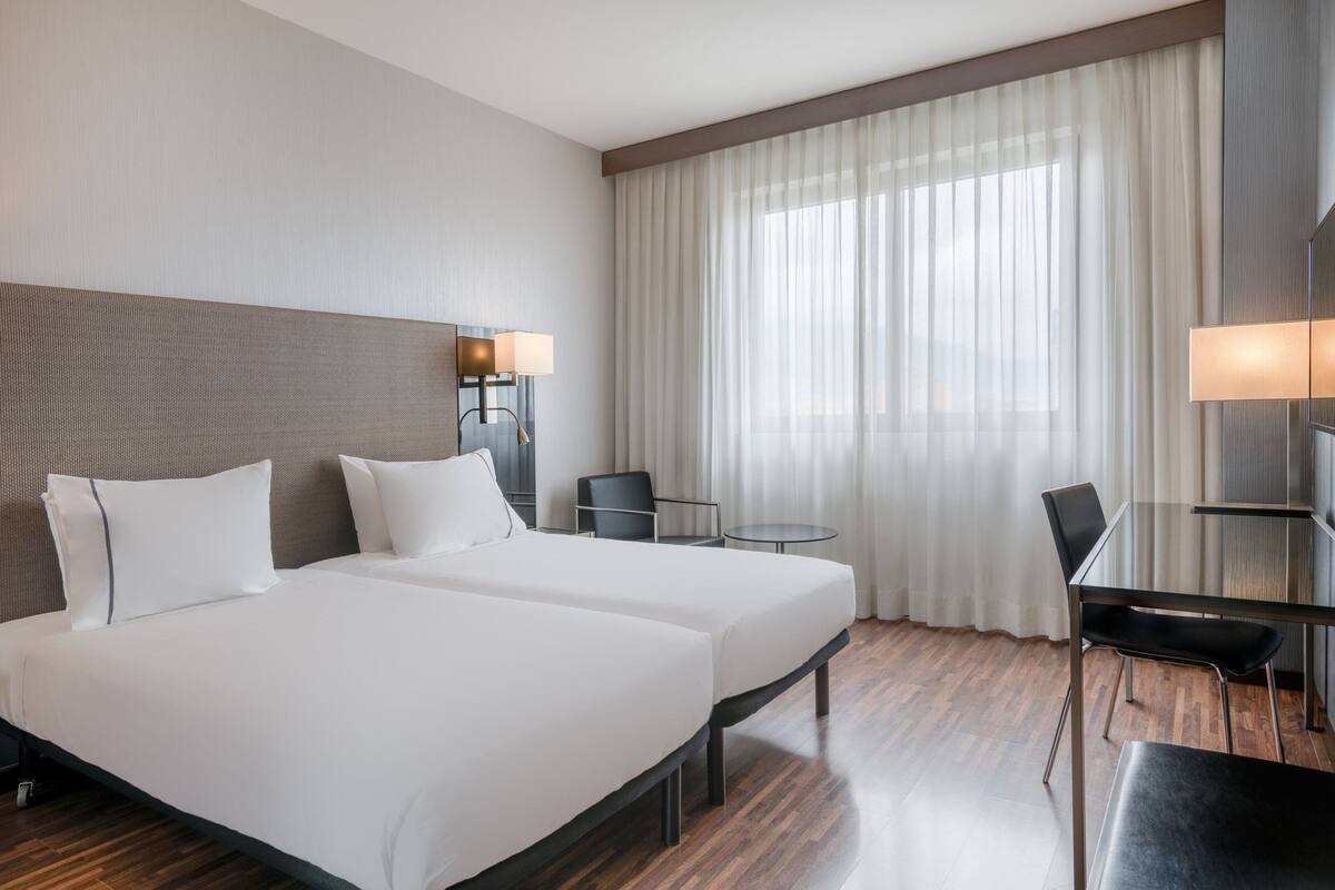 Habitación de hotel con dos camas, un escritorio, una silla y un televisor.